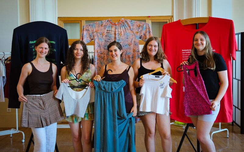 Fünf junge Frauen posieren mit Kleidungsstücken in der Hand vor der Ausstellung "tragbar?"