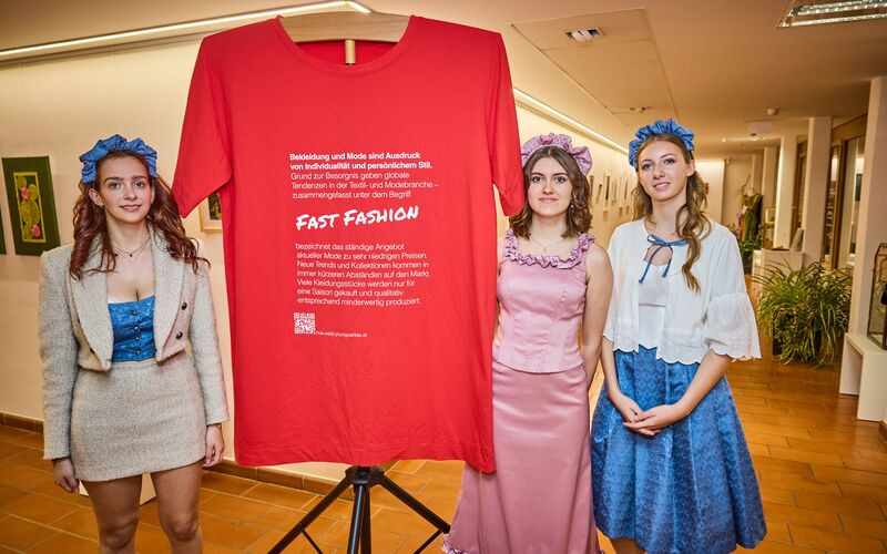 Drei Schülerinnen stehen neben einem XXL T-Shirt mit Fakten zum Thema Fast Fashion
