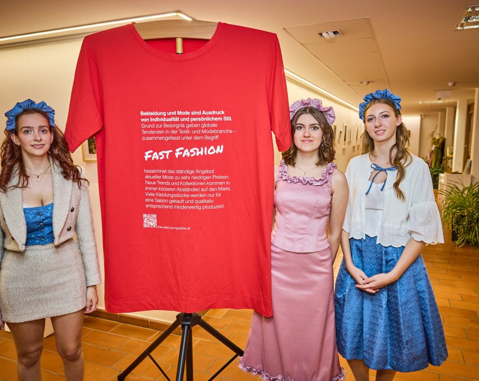 Drei Models posieren mit einem roten T-Shirt, auf dem das Thema "Fast Fashion" steht, während der Veranstaltung zur Bewusstseinsbildung.