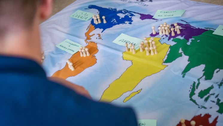Eine Person schaut auf ein Brettspiel mit einer Weltkarte, auf der Figuren und Notizen platziert sind, die verschiedene Regionen markieren.