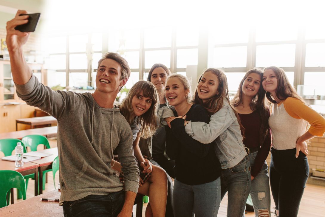 Eine Gruppe von jungen Leuten posiert glücklich für ein Selfie in einem Klassenraum.