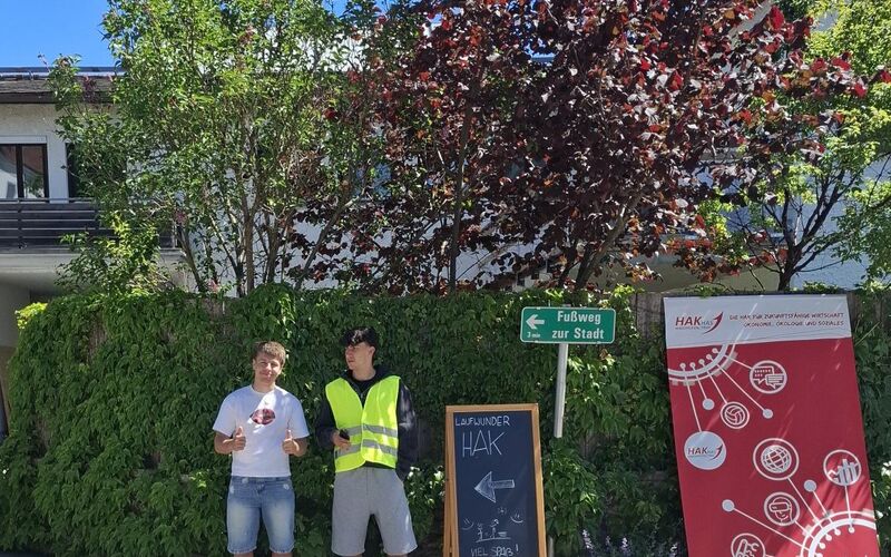 Zwei Schüler posieren vor einer Hecke und weisen mit einer Tafel auf den Weg für das LaufWunder hin.