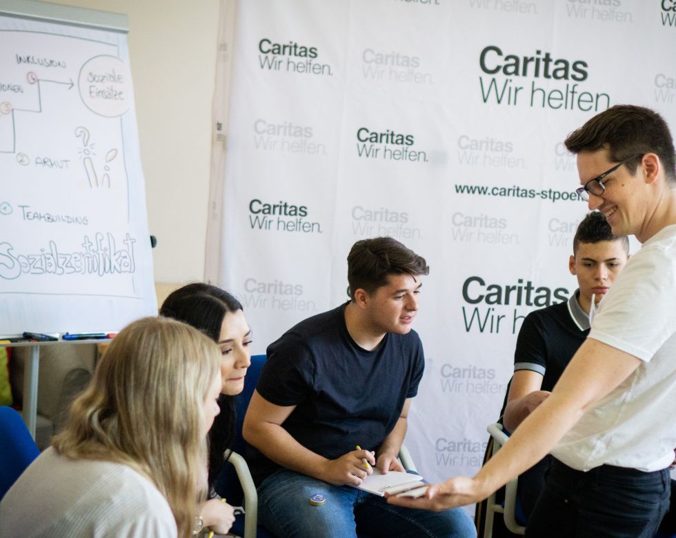 Eine Gruppe von jungen Menschen, die in einem Workshop von Caritas über soziale Themen diskutiert, während ein Moderator die Sitzung leitet.