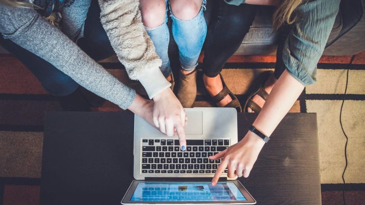 Drei Personen arbeiten zusammen an einem Laptop, ihre Hände zeigen auf den Bildschirm.