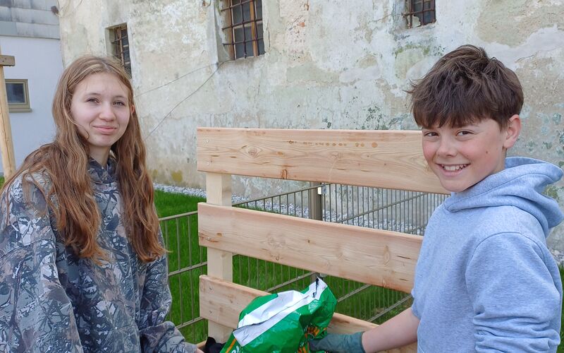 Zwei Schüler*innen beim Befüllen des Beetes mit einem Sack Erde.