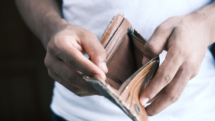 Eine Person hält einen leeren Geldbeutel in der Hand, was auf finanzielle Schwierigkeiten oder leere Taschen hindeutet.