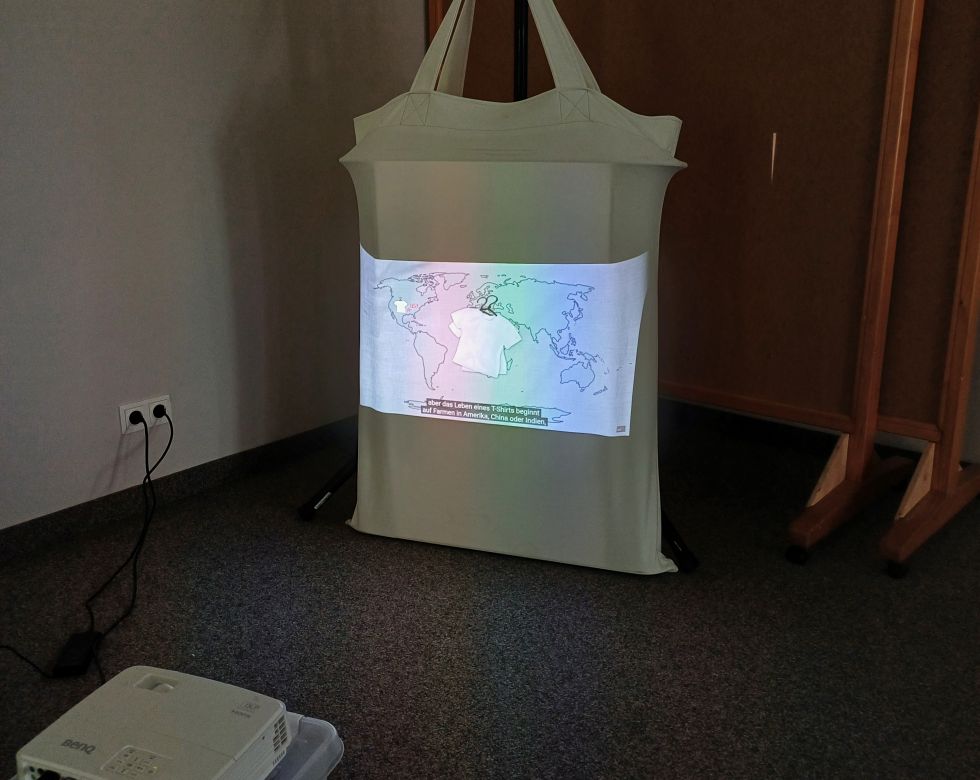 Ein Projektor zeigt eine farbige Karte auf einem weißen Bildschirm in einem Raum mit Teppichboden.