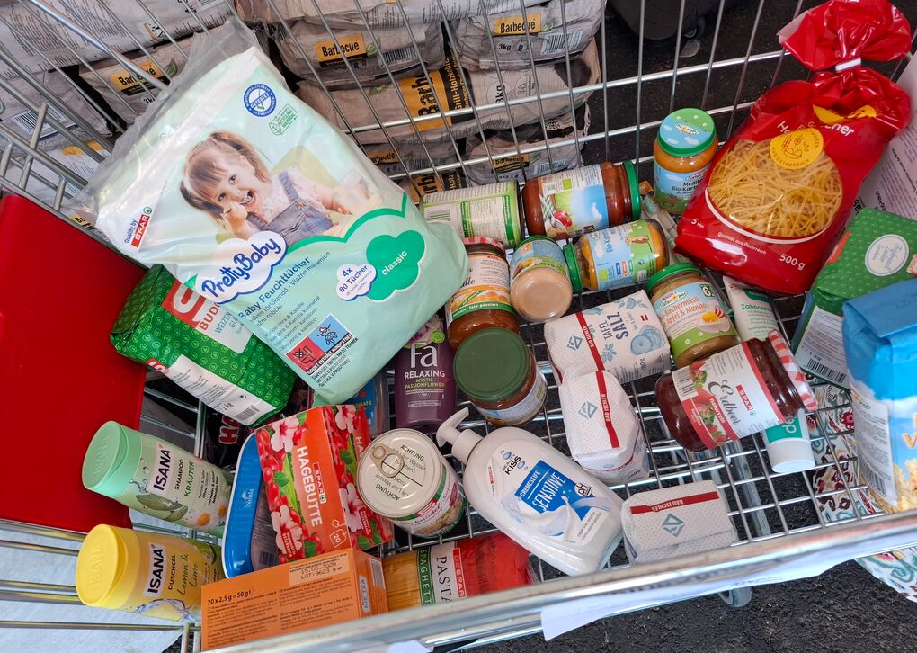 Ein Einkaufswagen mit unterschiedlichen Produkten - lang haltbare Lebensmittel, Hygieneartikel und Baby Feuchttücher.