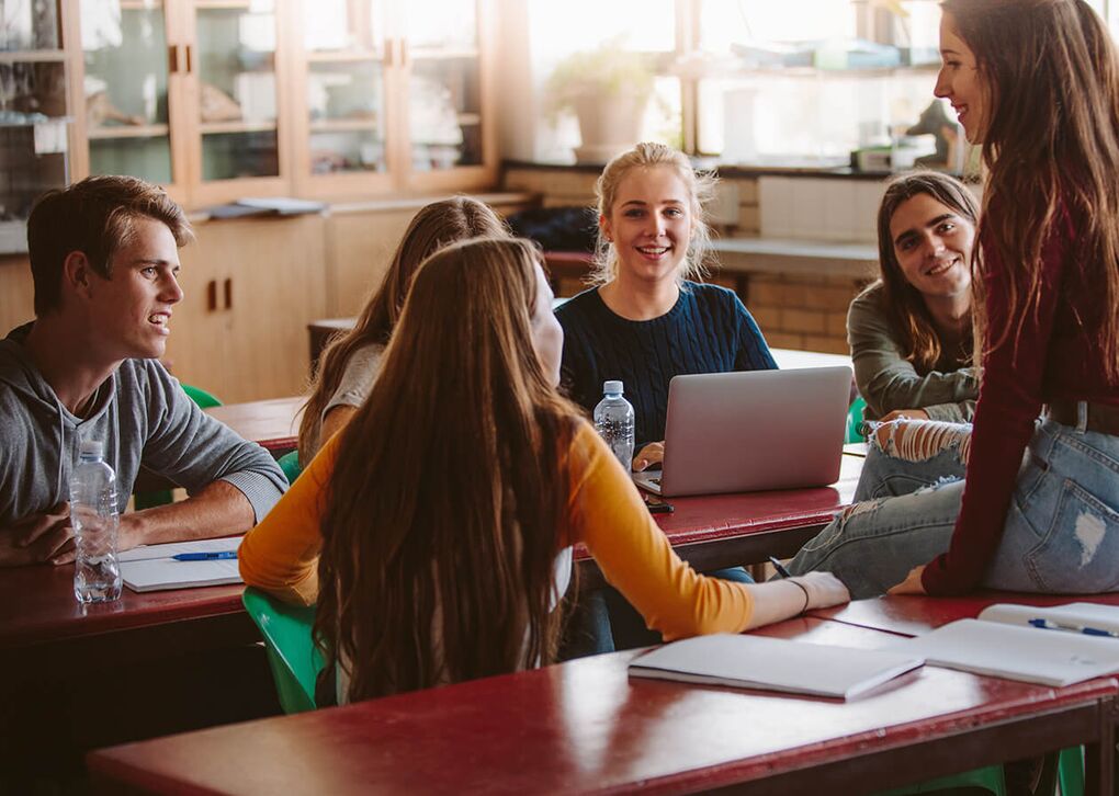 Eine Gruppe von Studenten versammelt sich am Tisch, diskutiert und arbeitet gemeinsam an einem Laptop.