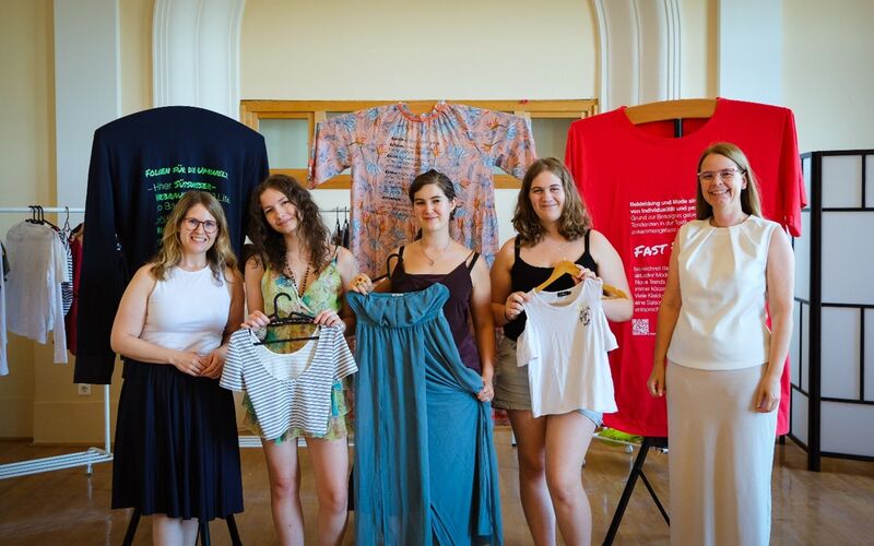 Fünf junge Frauen posieren mit Kleidungsstücken in der Hand vor der Ausstellung "tragbar?"