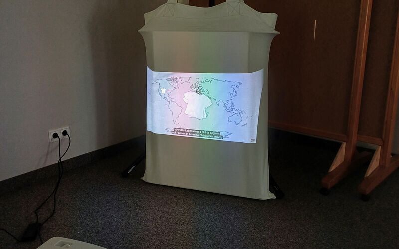 Ein Projektor zeigt eine farbige Karte auf einer großen weißen Tasche in einem Raum mit Teppichboden.
