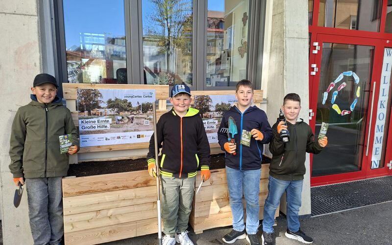 Vier Schüler mit Gartenwerkzeug vor den fertig aufgebauten Beeten.