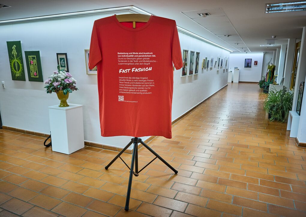 Ein Ausstellungsstück zu Fast Fashion. Es ist ein riesiges rotes T-Shirt mit weißem Text zu sehen.