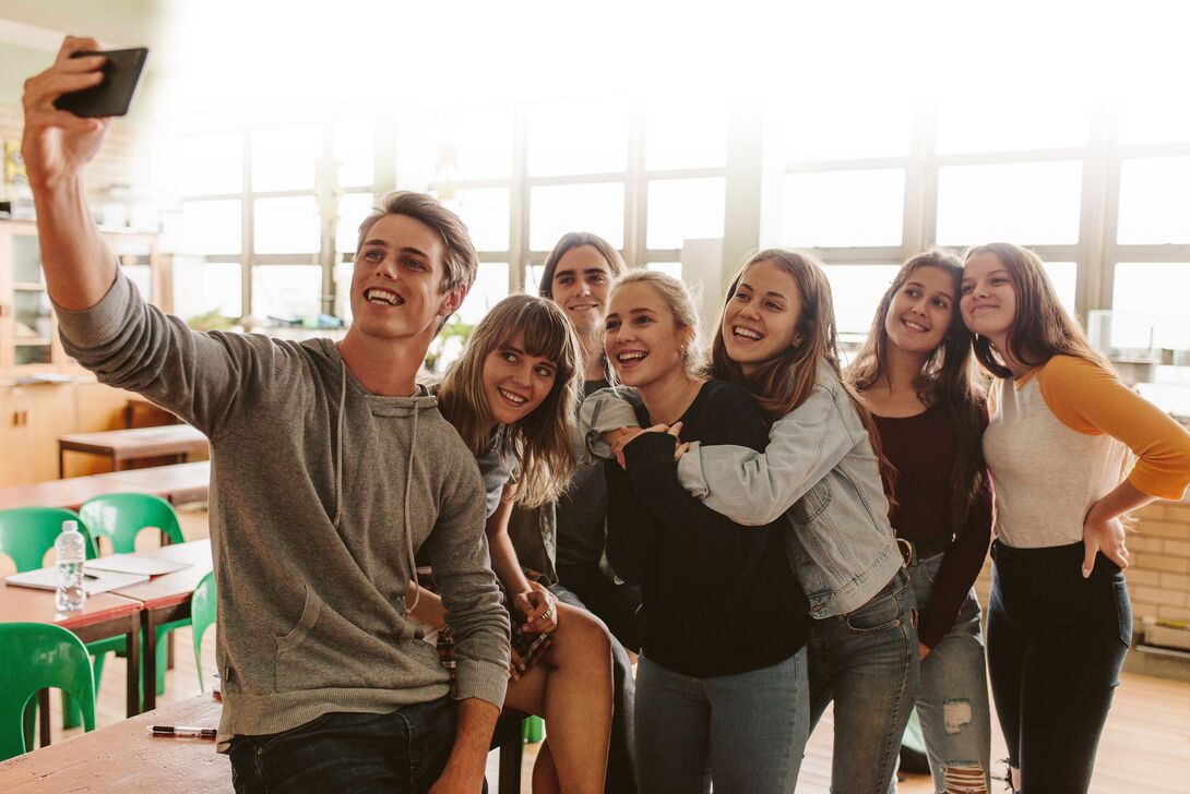 Eine Gruppe von jungen Leuten posiert glücklich für ein Selfie in einem Klassenraum.