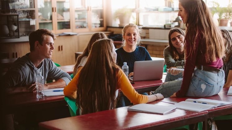 Eine Gruppe von Studenten versammelt sich am Tisch, diskutiert und arbeitet gemeinsam an einem Laptop.