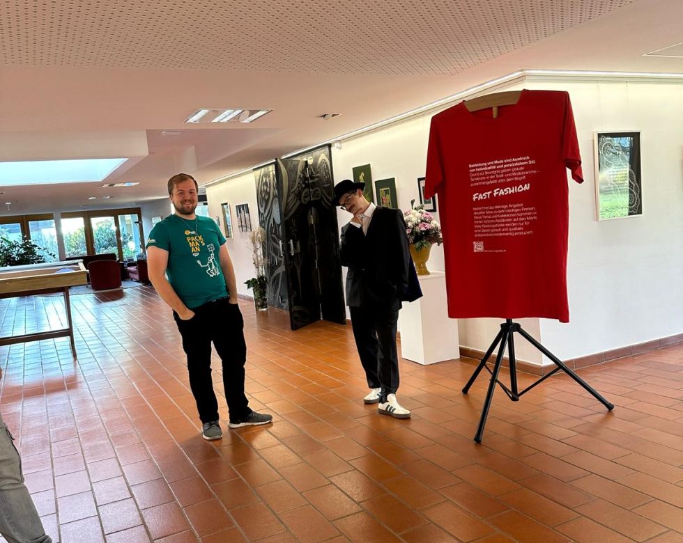 Eine Ausstellung mit einem roten T-Shirt über 'Fast Fashion' und zwei Männern in einem modernen Raum.