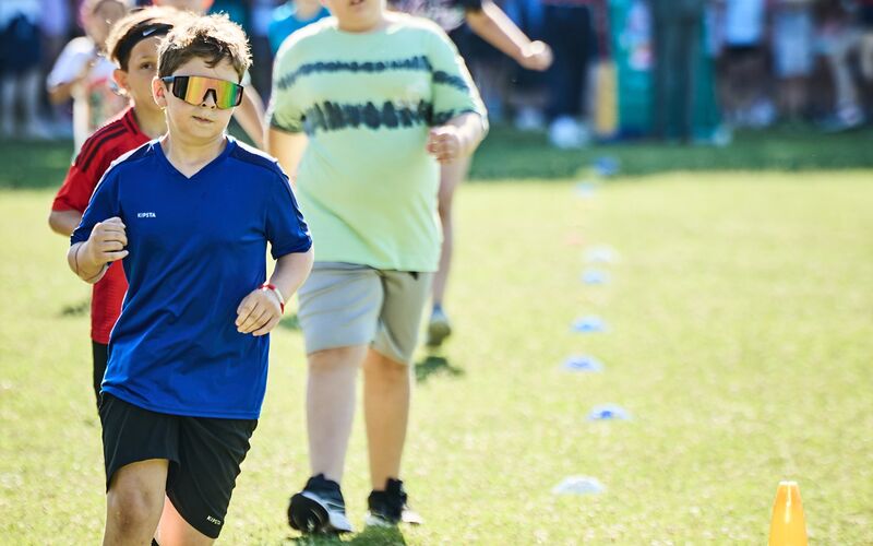 Ein Junge im Sportgewand und reflektierender Sonnenbrille läuft beim LaufWunder. Dahinter sind weitere laufenden Kinder zu sehen.
