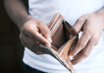 Eine Person hält einen leeren Geldbeutel in der Hand, was auf finanzielle Schwierigkeiten oder leere Taschen hindeutet.