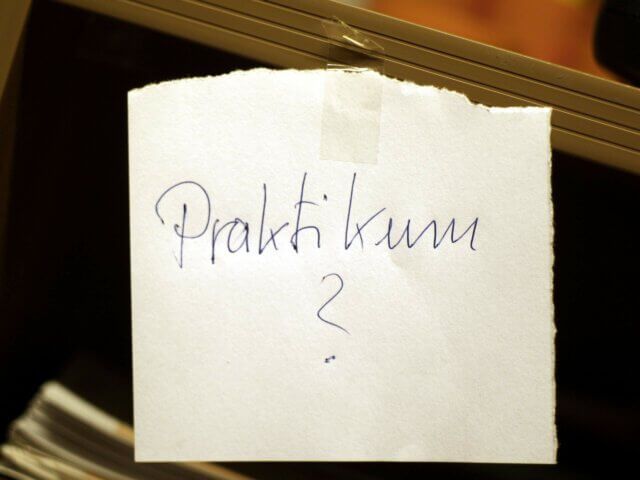 Ein handgeschriebener Zettel, auf dem 'Praktikum ?' steht, hängt an einem Schrank.