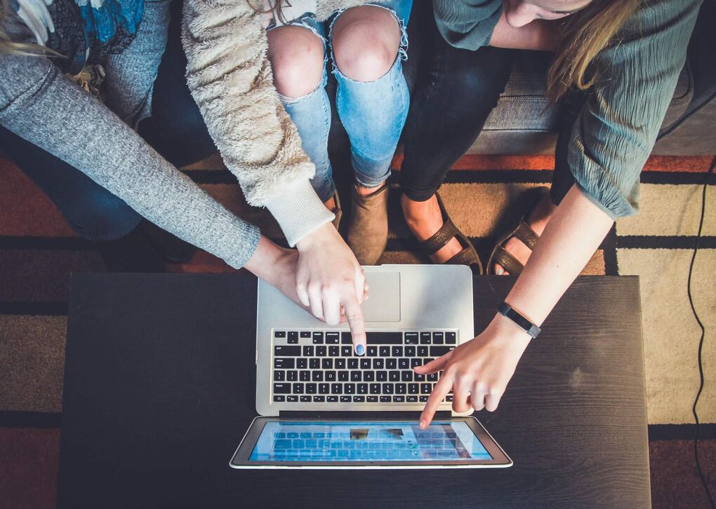 Drei Personen arbeiten zusammen an einem Laptop, ihre Hände zeigen auf den Bildschirm.