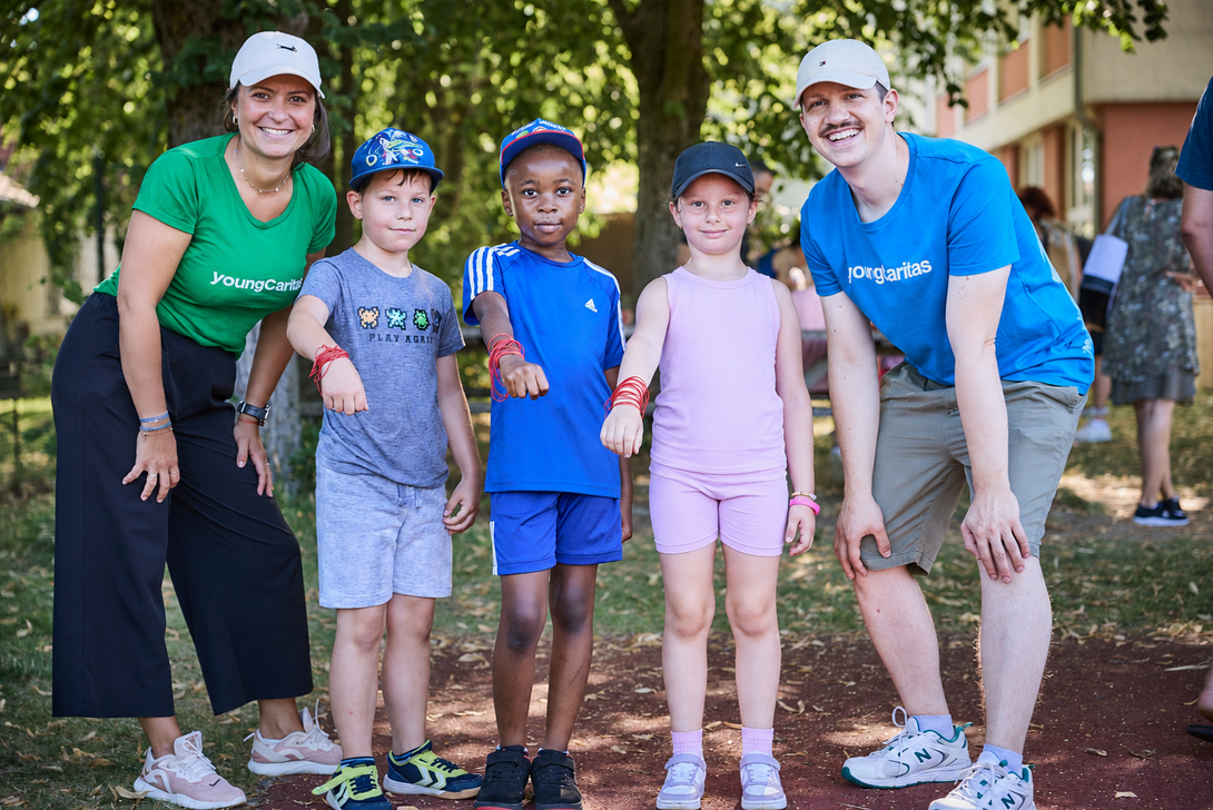 Drei Kinder posieren zwischen zwei youngCaritas Referent*innen und zeigen anhand von Gmmibändern, wie viele Runden sie beim LaufWunder geschafft haben.