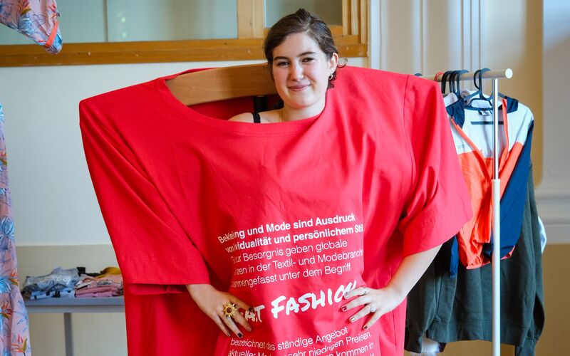 Eine junge Frau posiert mit einem überdimensional großen T-Shirt zum Thema Fast Fashion.