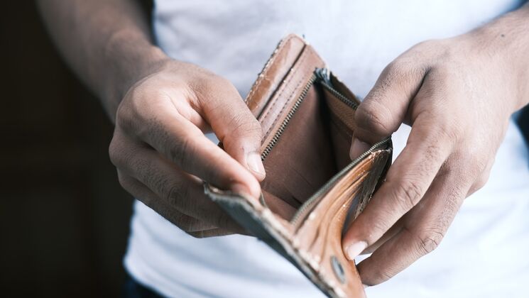 Eine Person hält einen leeren Geldbeutel in der Hand, was auf finanzielle Schwierigkeiten oder leere Taschen hindeutet.