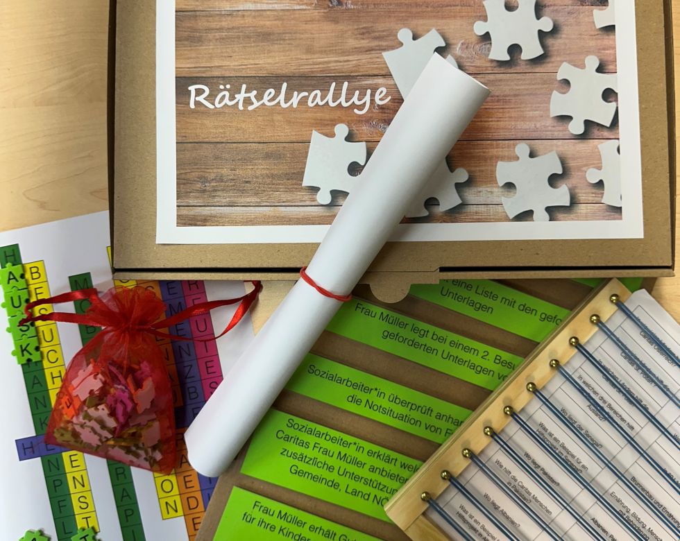 Ein aufgeschlagenes Paket mit Materialien für eine Rätselrallye von youngCaritas, darunter Hinweise, Gutscheine und ein Dokument.