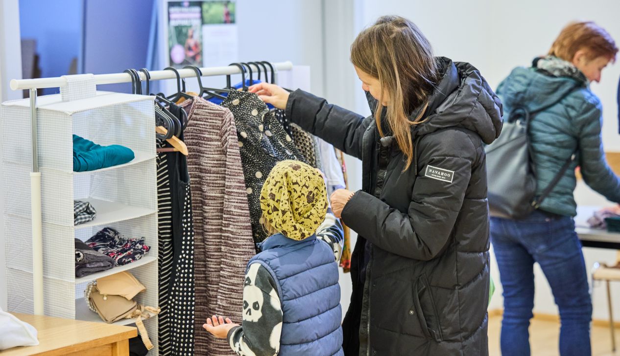 Mutter mit Kind schaut sich Kleidungsstücke bei der Tauschbar an