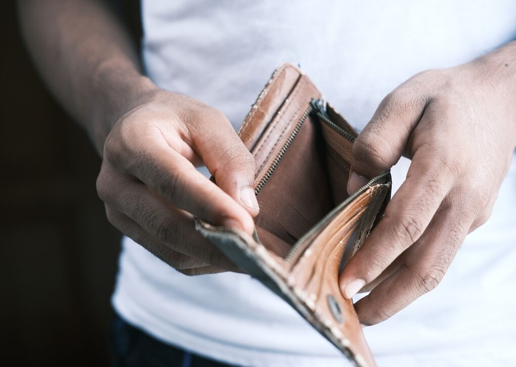 Eine Person hält einen leeren Geldbeutel in der Hand, was auf finanzielle Schwierigkeiten oder leere Taschen hindeutet.