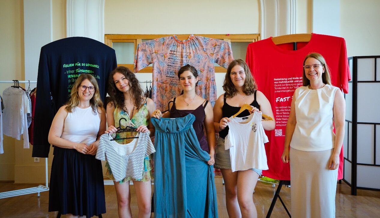 Fünf junge Frauen posieren mit Kleidungsstücken in der Hand vor der Ausstellung "tragbar?"