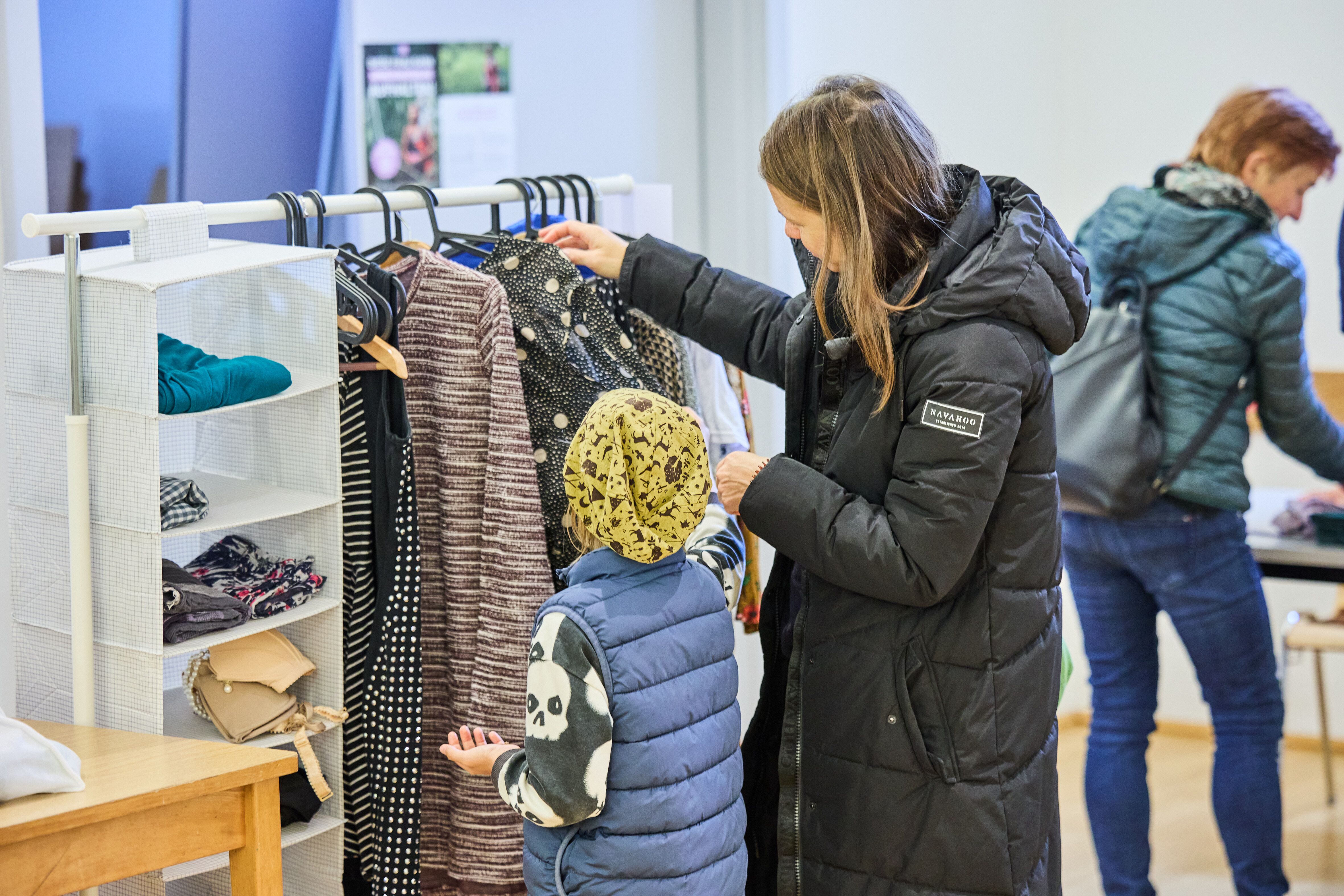 Mutter mit Kind schaut sich Kleidungsstücke bei der Veranstaltung "tauschbar" an.